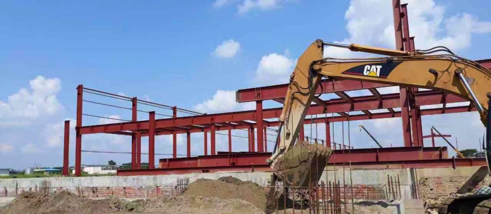 A photo of steel frame construction by Myanmar Yi Jin, a steel construction company. The image shows a building foundation with red steel beams and columns and an excavator.